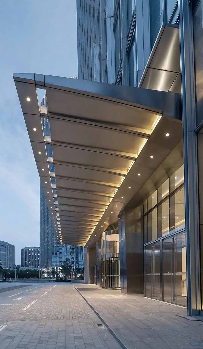 Glass canopy with stainless steel supports extending over a contemporary entrance
