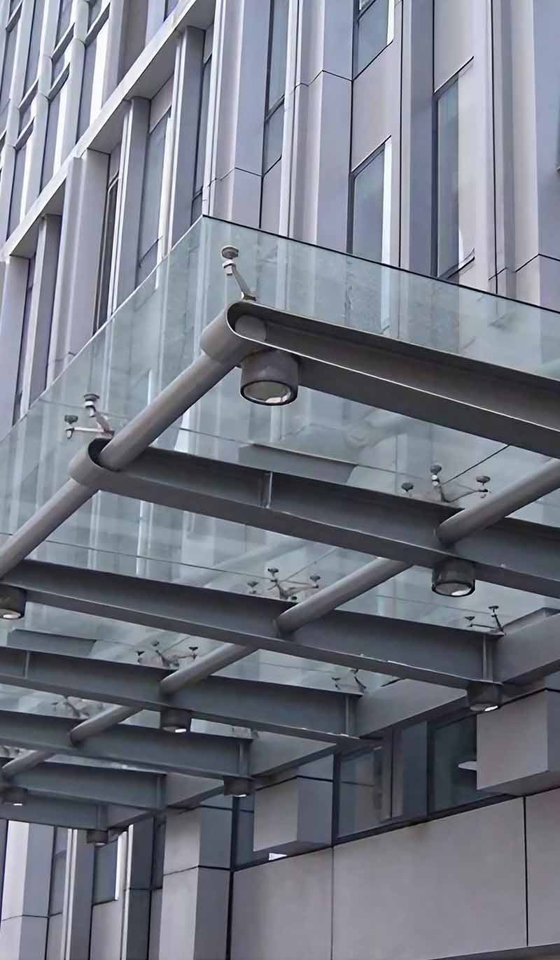 Glass canopy supported by a stainless steel frame along a building facade