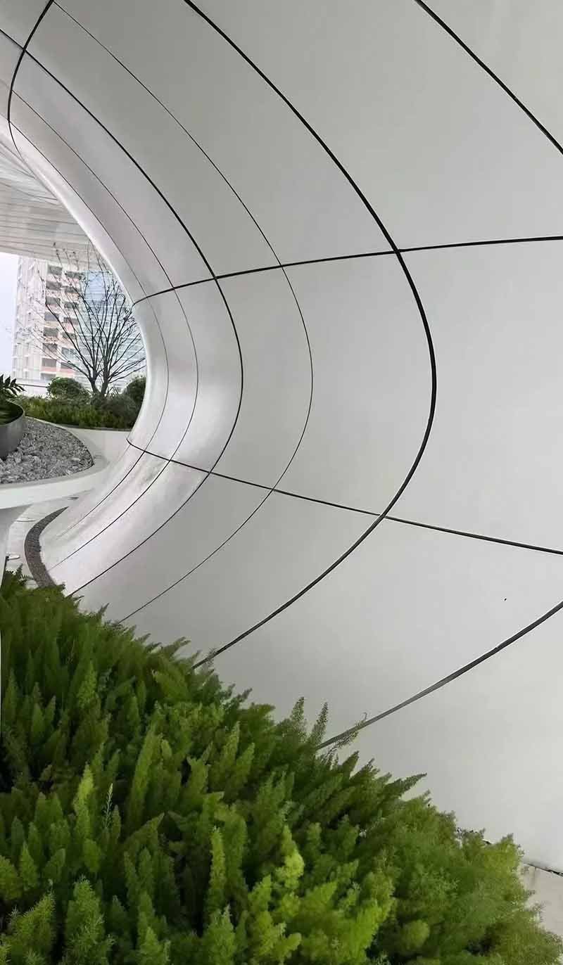 Double-curved aluminium facade panels creating layered contours across a modern building exterior